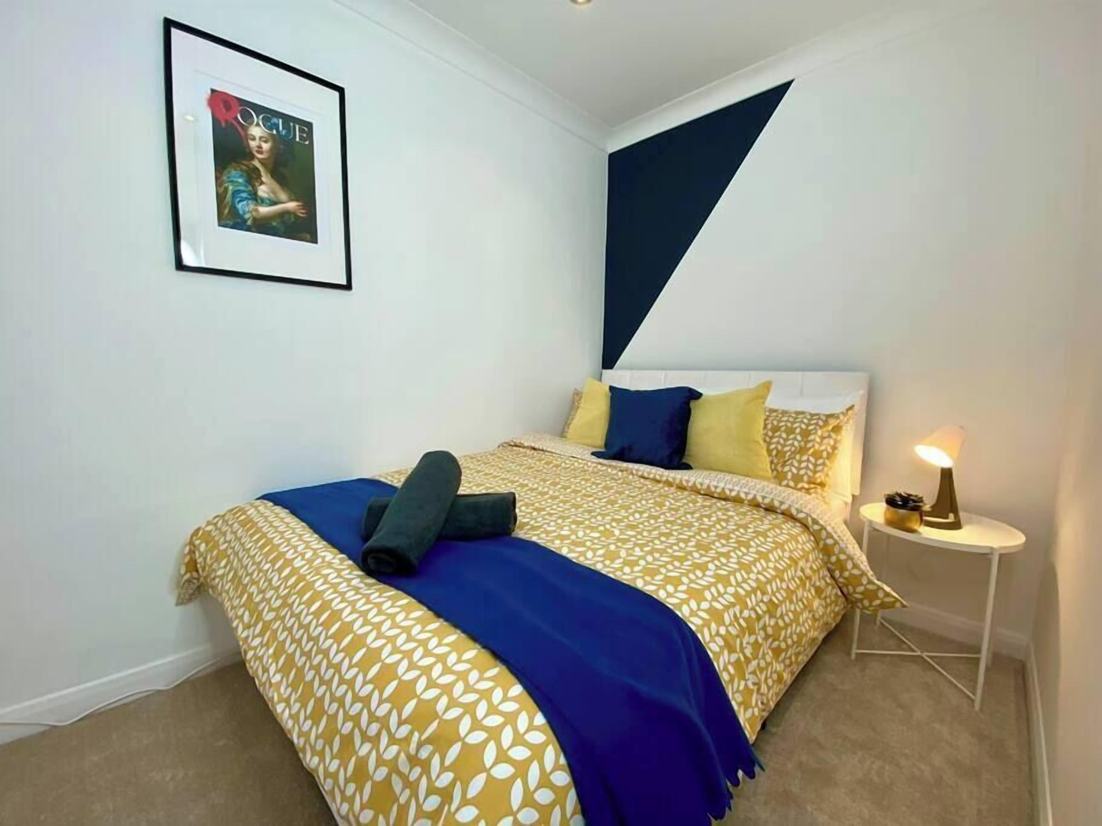 A bedroom with a bed, pillows, a bedside table with a lamp, and a framed picture on the wall.
