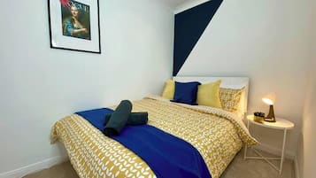 A bedroom with a bed, pillows, a bedside table with a lamp, and a framed picture on the wall.
