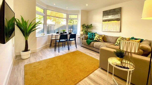A modern living room with a sofa, a coffee table, a dining table with chairs, and a large window.