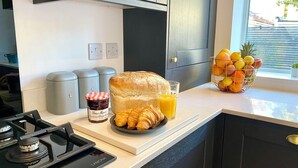 A kitchen with a gas stove, a loaf of bread, croissants, a glass of orange juice, and a fruit bowl.