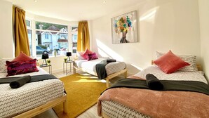 A modern hotel room with two beds, a large window with curtains, a small table with a lamp, and a painting on the wall.