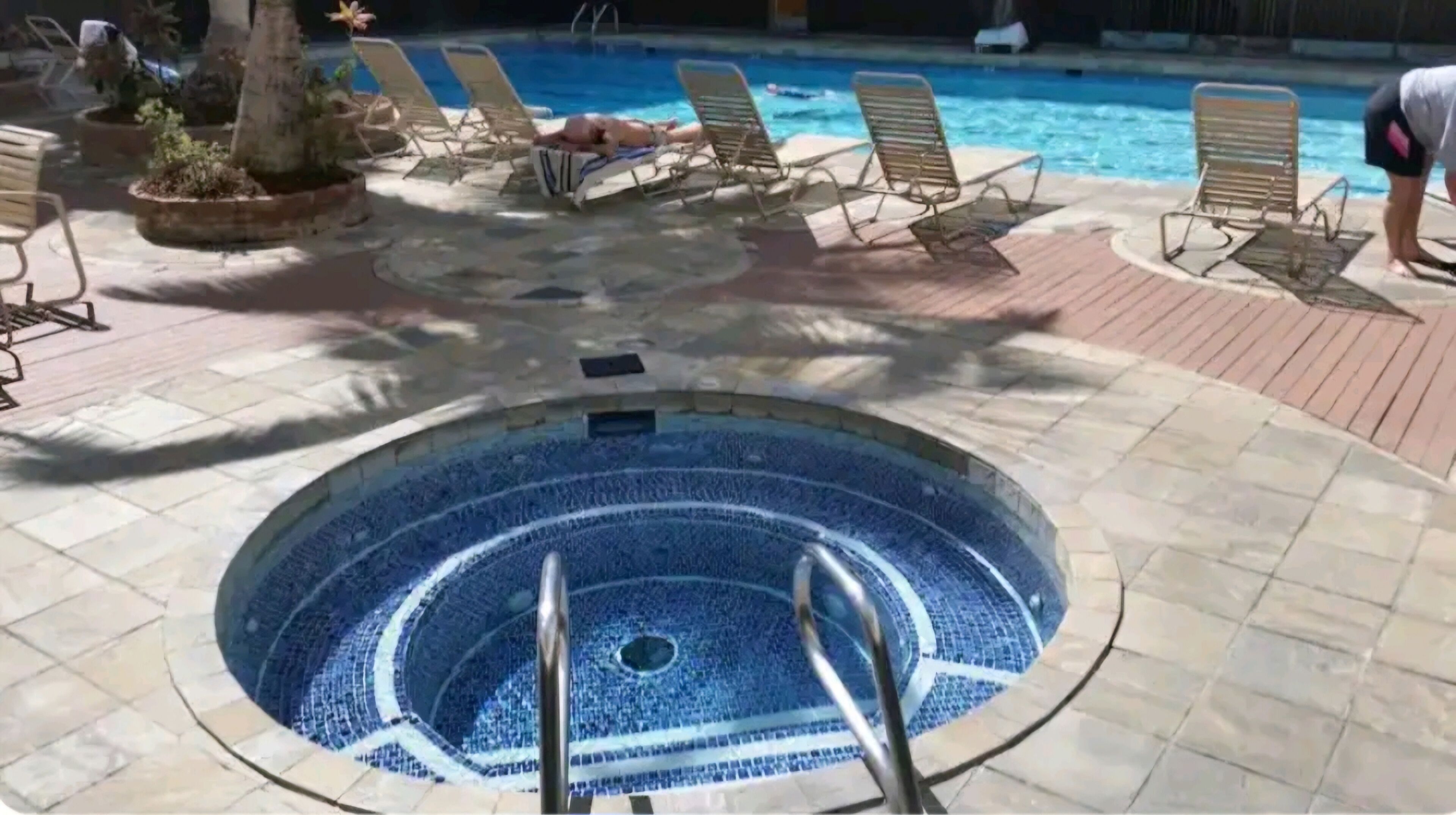 A circular pool with a tiled edge, surrounded by lounge chairs and potted plants.