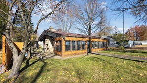 Un edifici de fusta amb grans finestres, un pati amb gespa i arbres.