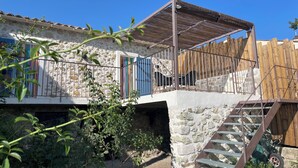 A stone building with a balcony, a wooden fence, and a staircase leading to an upper level. - Maison de Caractère (Peyroules)