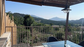 A balcony with a glass table and chairs, a metal railing, and a view of a hilly landscape. - Maison de Caractère (Peyroules)