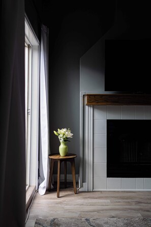 A room with a fireplace, a window with curtains, and a small table with a vase. - Summit Rails | 3BR Loft | Unique Canmore Character | Walk to Everything | Sleeps 6 (Canmore)