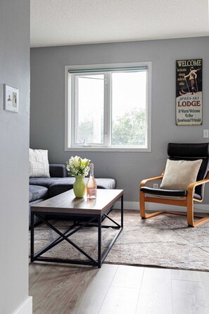 Una sala de estar moderna con un sofá gris, una mesa de centro de madera, un jarrón verde y un sillón de cuero negro.