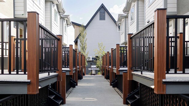 A narrow pathway flanked by wooden fences and white buildings with black railings. - Summit Rails | 3BR Loft | Unique Canmore Character | Walk to Everything | Sleeps 6 (Canmore)