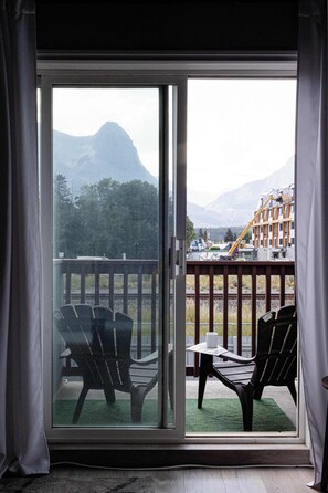 A room with a sliding glass door leading to an outdoor deck with chairs and a table. - Summit Rails | 3BR Loft | Unique Canmore Character | Walk to Everything | Sleeps 6 (Canmore)