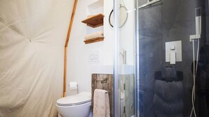 A compact bathroom with a toilet, a glass shower enclosure, and wooden shelves. - Cody Peak Dome, Stunning Views! Near Cody, WY and Yellowstone National Park (Cody)