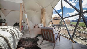 A cozy interior of a tent with a wooden chair, a bed, and a view of the outdoors. - Cody Peak Dome, Stunning Views! Near Cody, WY and Yellowstone National Park (Cody)