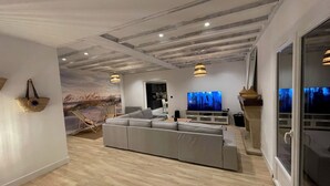 Un salon moderne doté d’un grand canapé d’angle gris, d’un téléviseur à écran plat et d’un coin repas avec une table et des chaises.