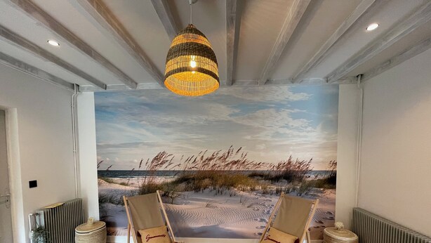 Une pièce décorée d’une fresque représentant une plage, avec deux chaises de plage, une lampe en osier et un radiateur.