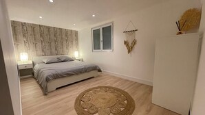 Une chambre à coucher comprenant un lit, des tables de chevet, une fenêtre, un élément de décoration fixé au mur et un tapis rond en fibres tressées.