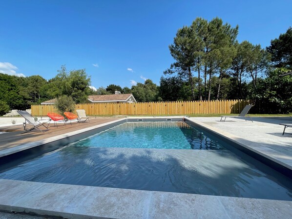 A rectangular swimming pool with a wooden deck and lounge chairs. - Vacation villa with a pool and garden between the estuary and the ocean. (Talais)
