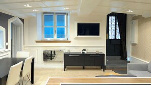 Een moderne woonkamer met een eethoek, een zwarte entertainmentkast, een televisie boven een raam en een trap naar een hoger niveau.