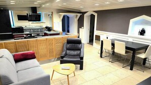 Een moderne woonkamer met een grijze bank, een zwarte leren fauteuil, een houten salontafel en een eetgedeelte met een zwarte tafel en witte stoelen.