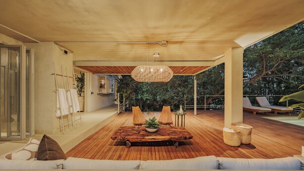 A modern outdoor living area with a wooden deck, a dining table with chairs, and a large hanging light fixture.