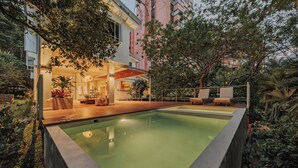 A modern outdoor pool area with a wooden deck, lounge chairs, and a well-lit patio.