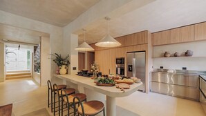 A modern kitchen with a central island, bar stools, stainless steel appliances, and wooden cabinets.