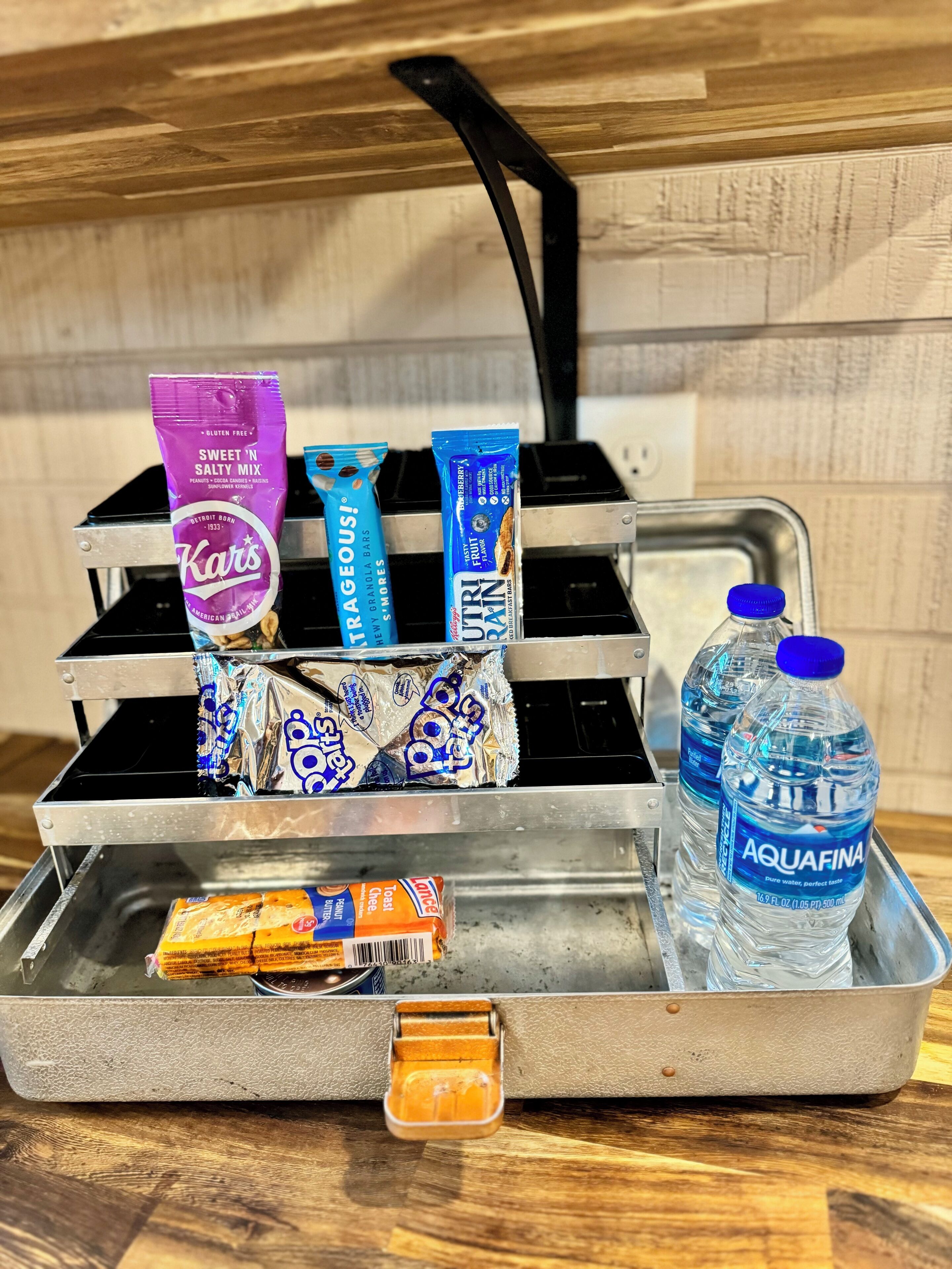 En metalbakke med snacks, en vandflaske og en beholder.