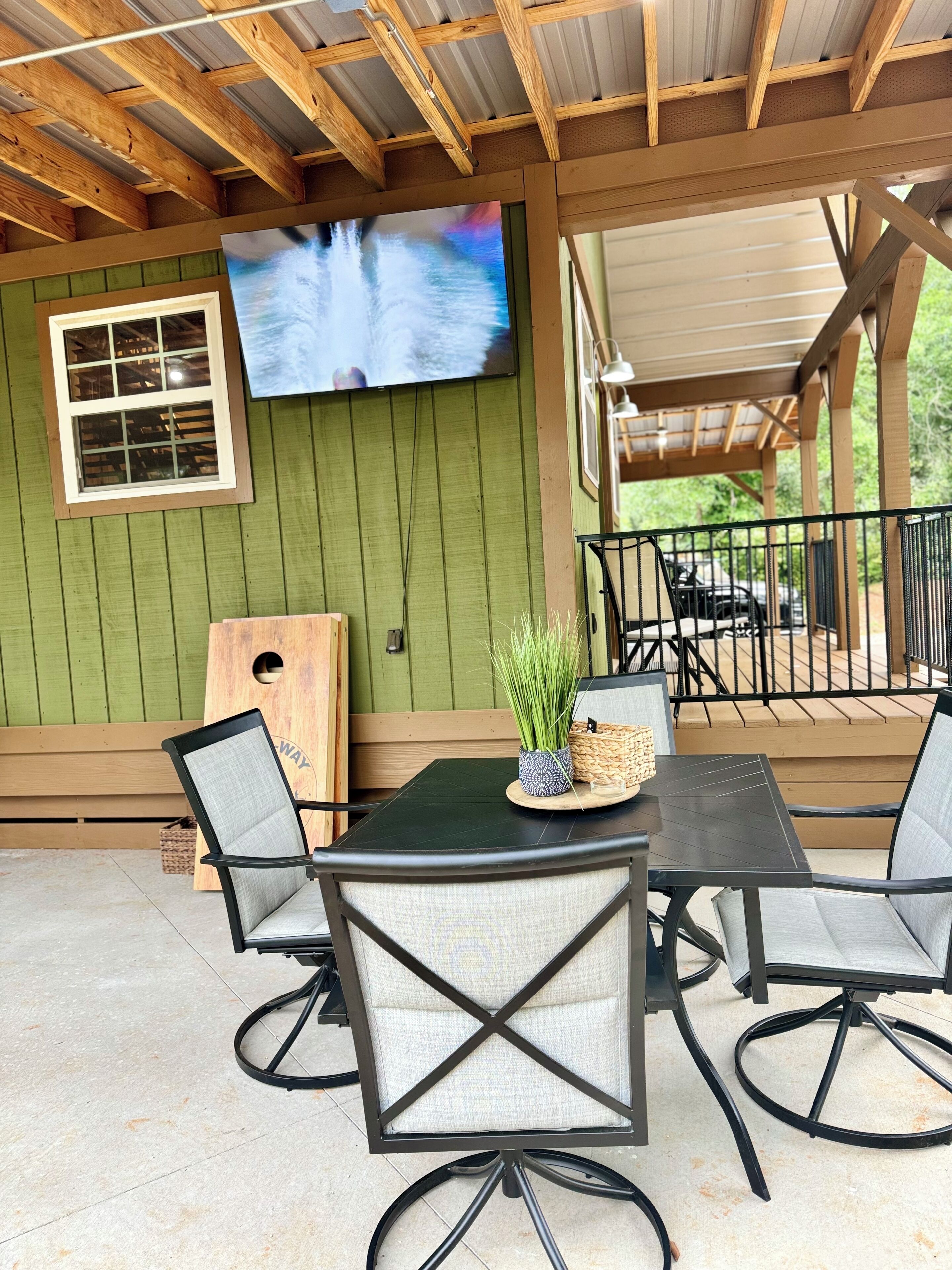 Un patio exterior con una mesa y sillas, un televisor montado en la pared y una tabla de madera.