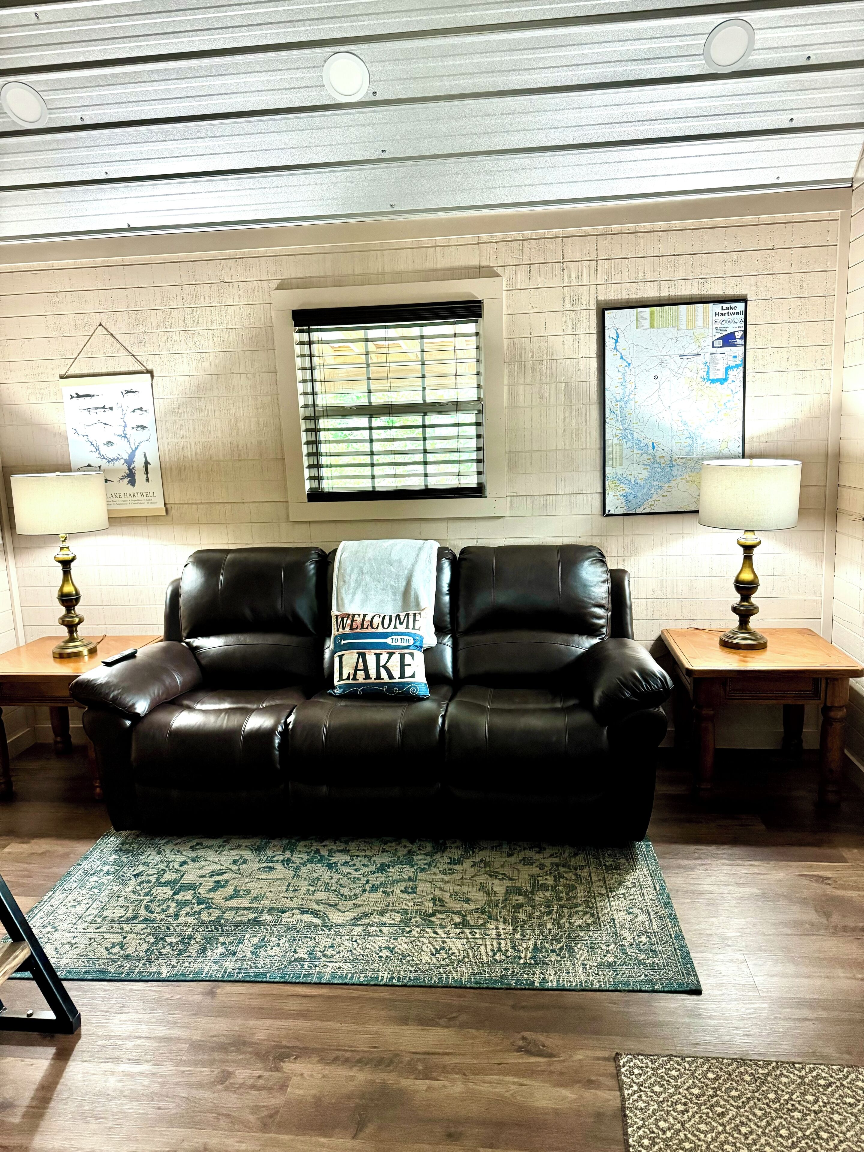 A living room with a leather couch, two lamps, a rug, a map on the wall, and a window with blinds.