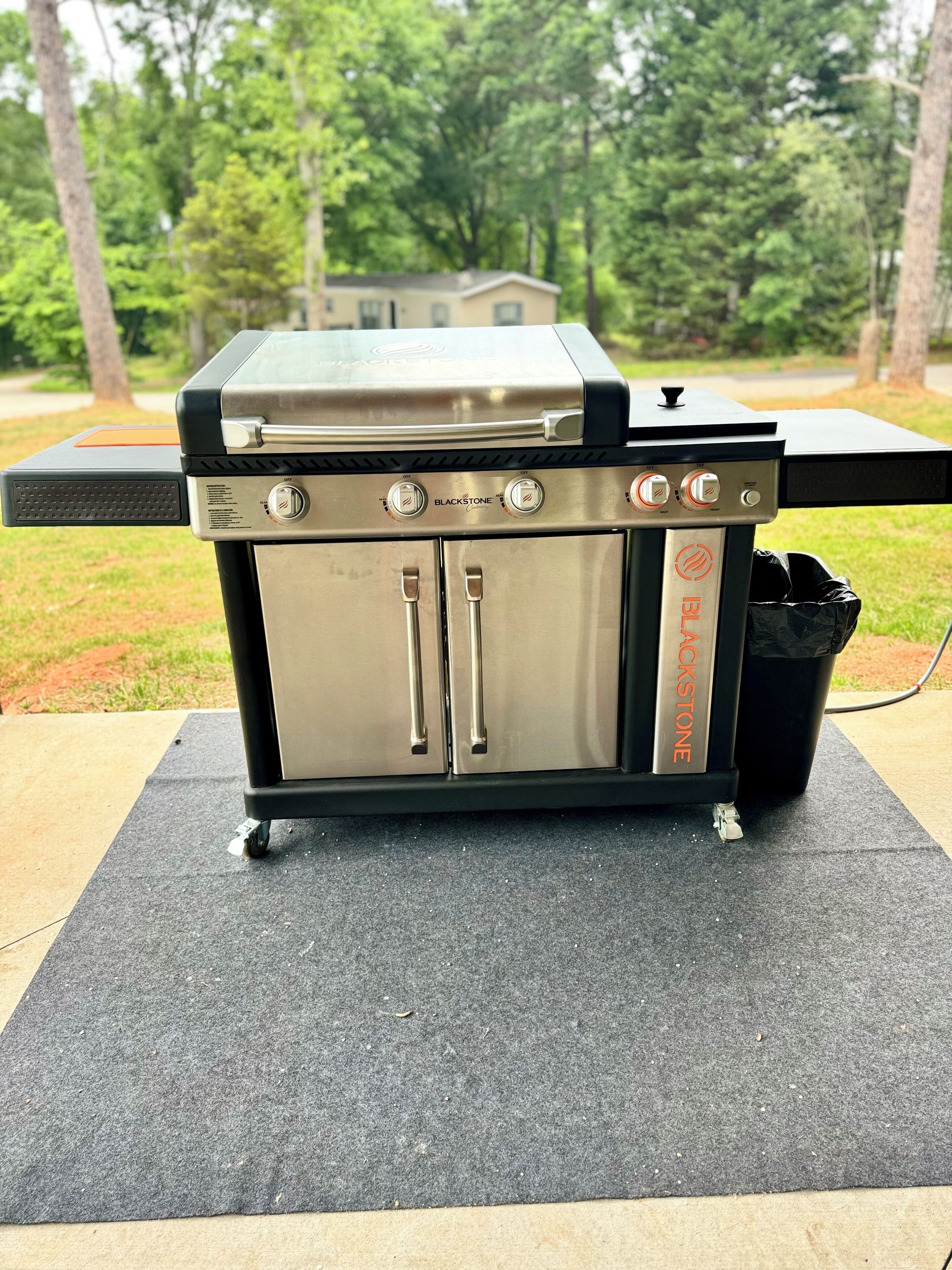 Una parrilla portátil con dos compartimentos de acero inoxidable y una pantalla digital, colocada sobre un tapete al aire libre.