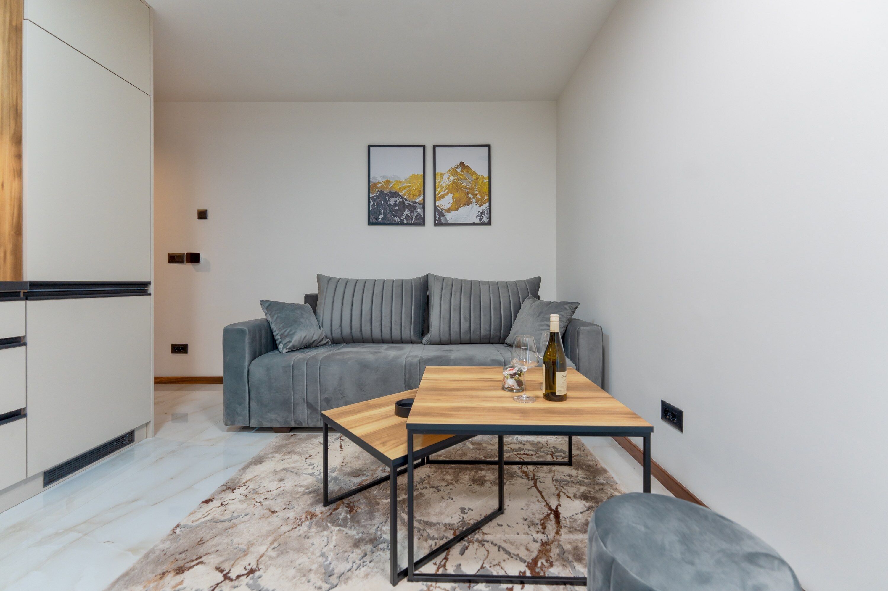 A modern living room with a grey sofa, a wooden coffee table, and two framed pictures on the wall.