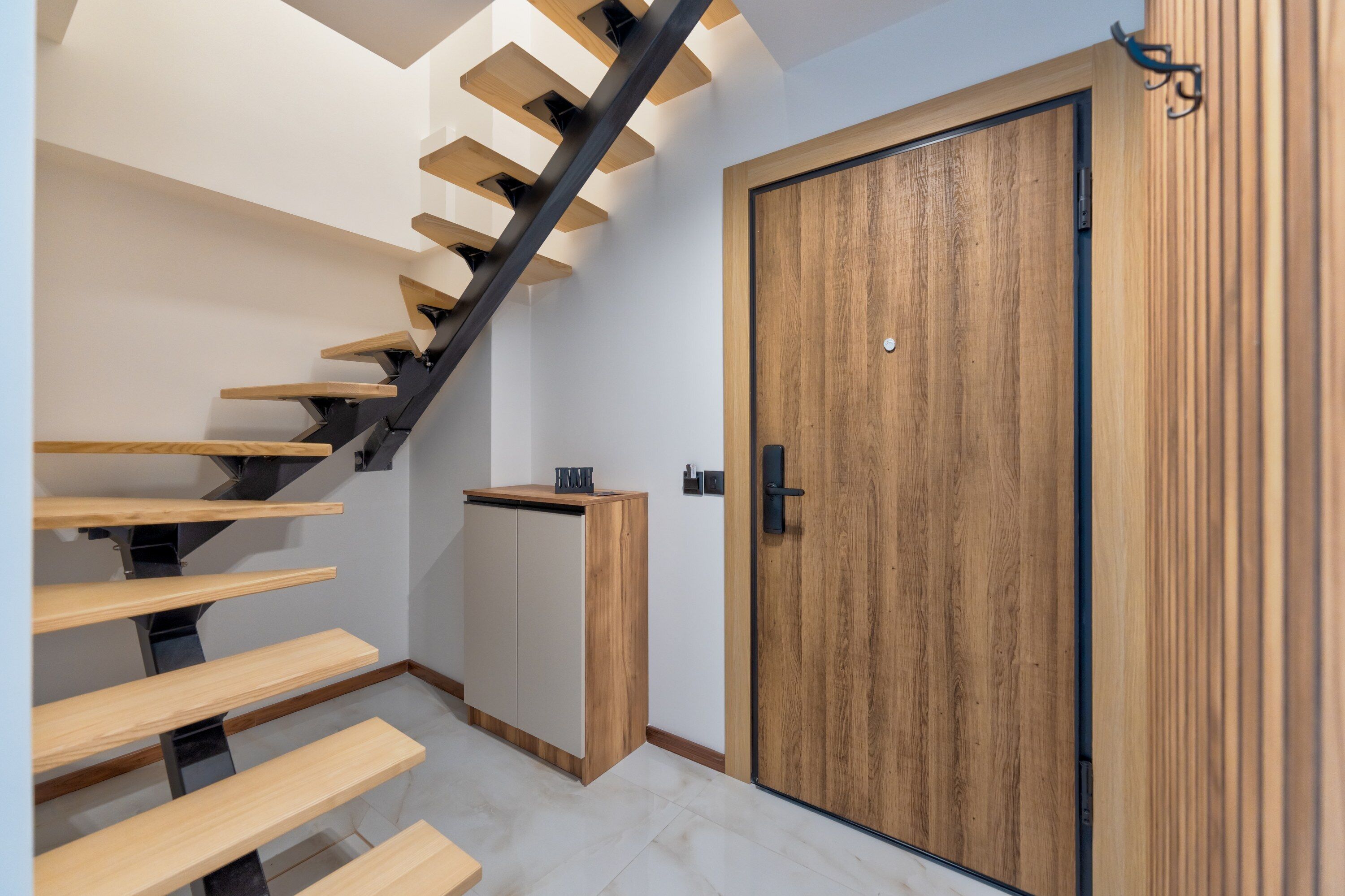 Una escalera moderna con escalones de madera y barandillas negras, que lleva a una puerta de madera con picaporte negro.