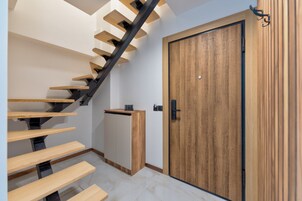 Una escalera moderna con escalones de madera y barandillas negras, que lleva a una puerta de madera con picaporte negro.