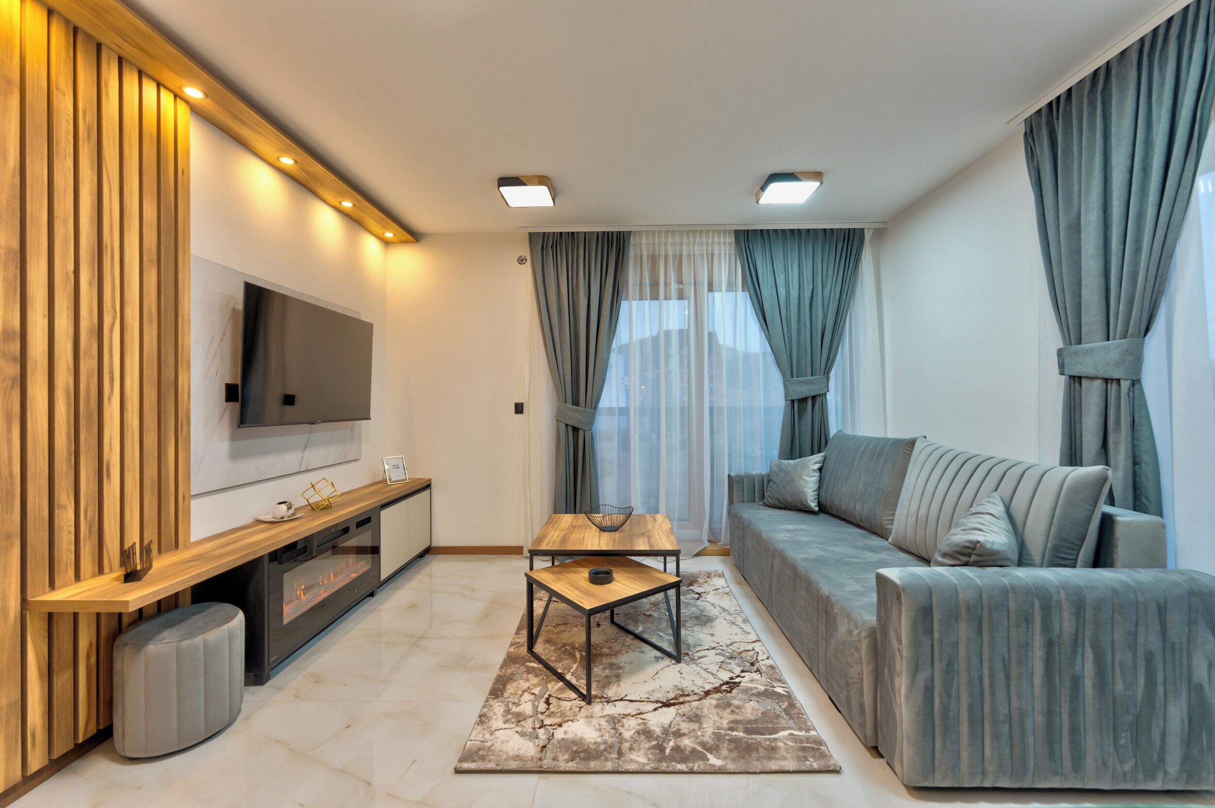 A modern living room with a flat-screen TV, wooden paneling, a sofa, a coffee table, and a patterned rug.