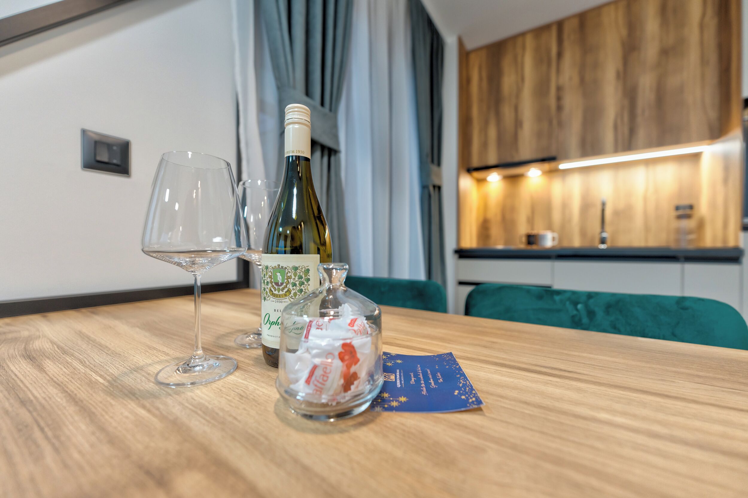 A wooden table with a bottle of wine, two wine glasses, and a small bowl of snacks.