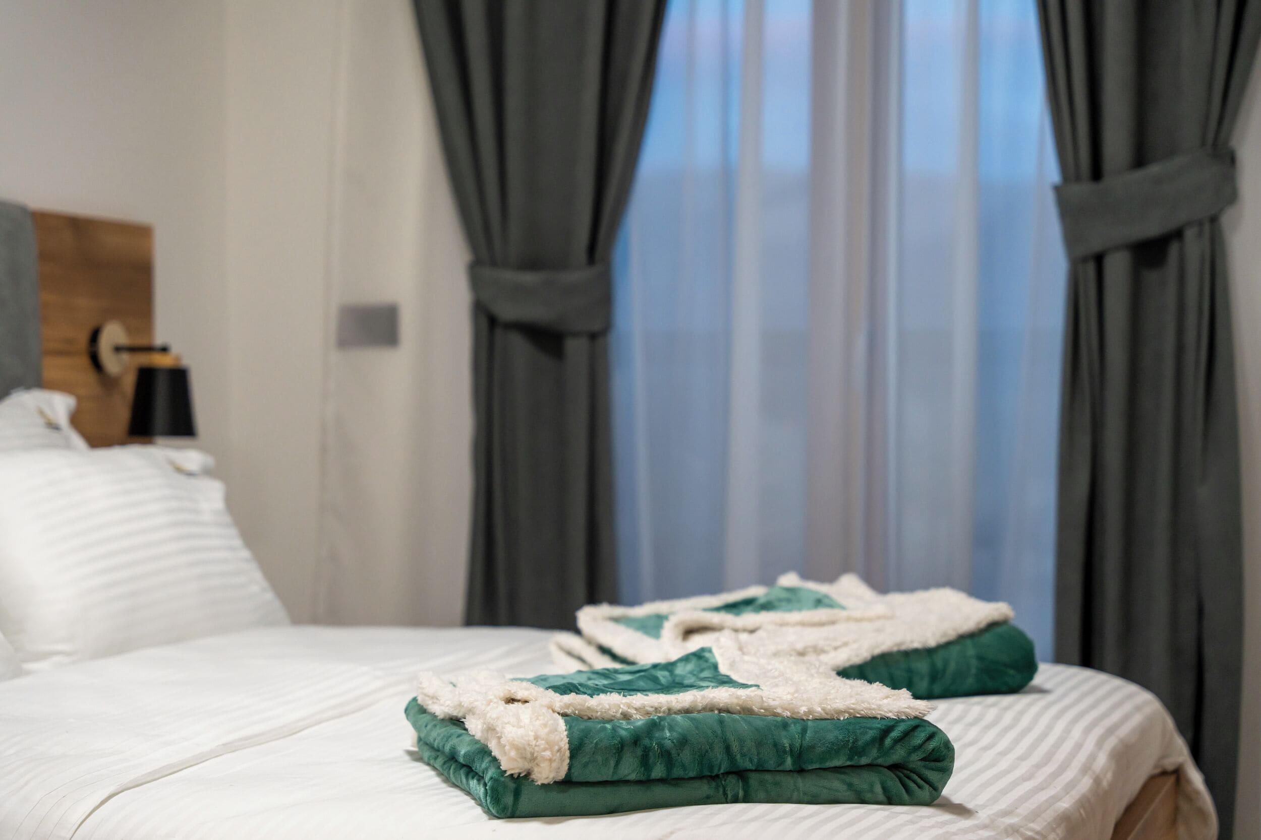 Una cama bien hecha con ropa de cama verde y blanca, un cabecero de madera y una ventana con cortinas.
