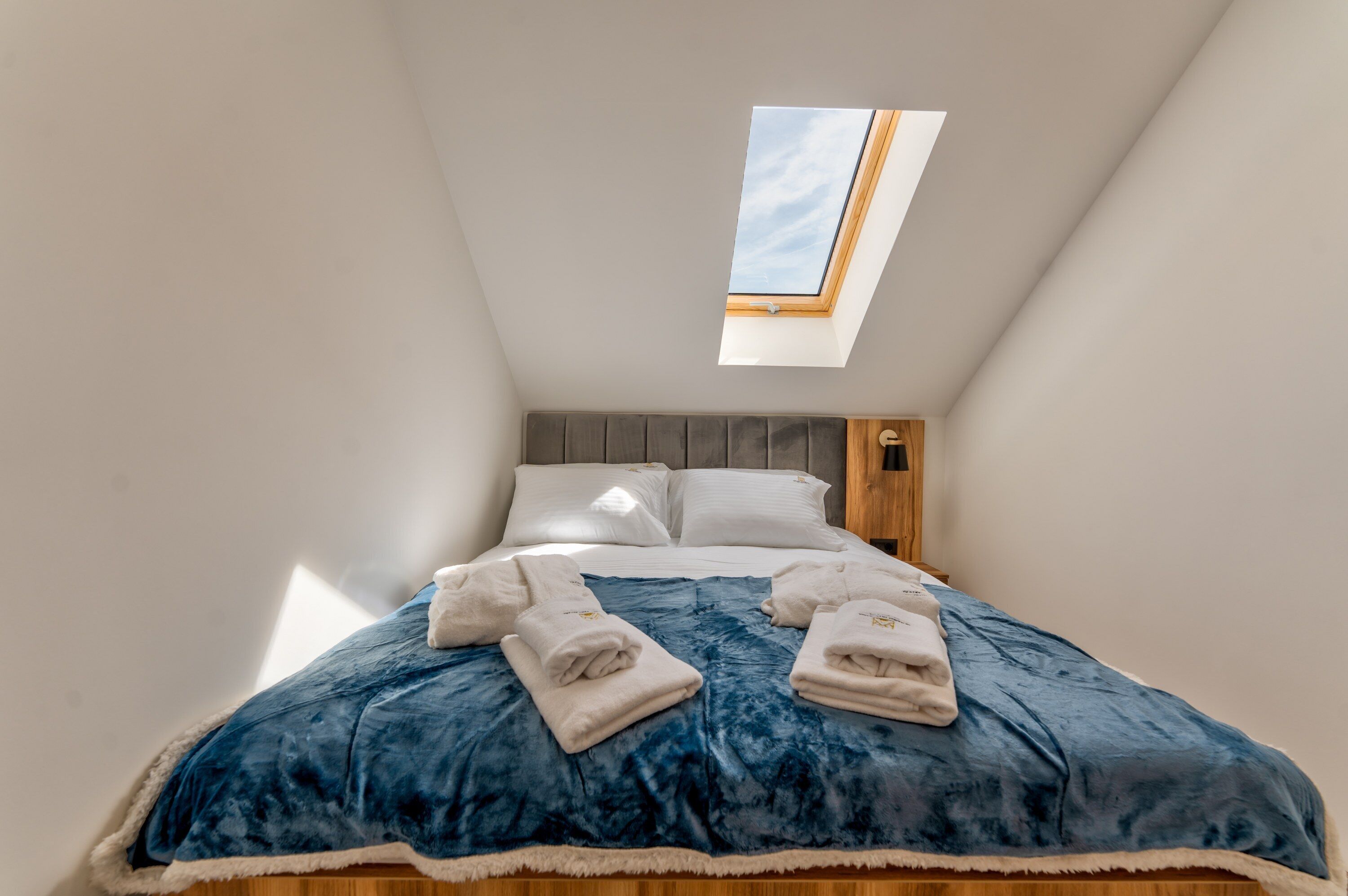 Ein Schlafzimmer mit Dachfenster, einem Bett mit blauer Decke und zwei Handtüchern.