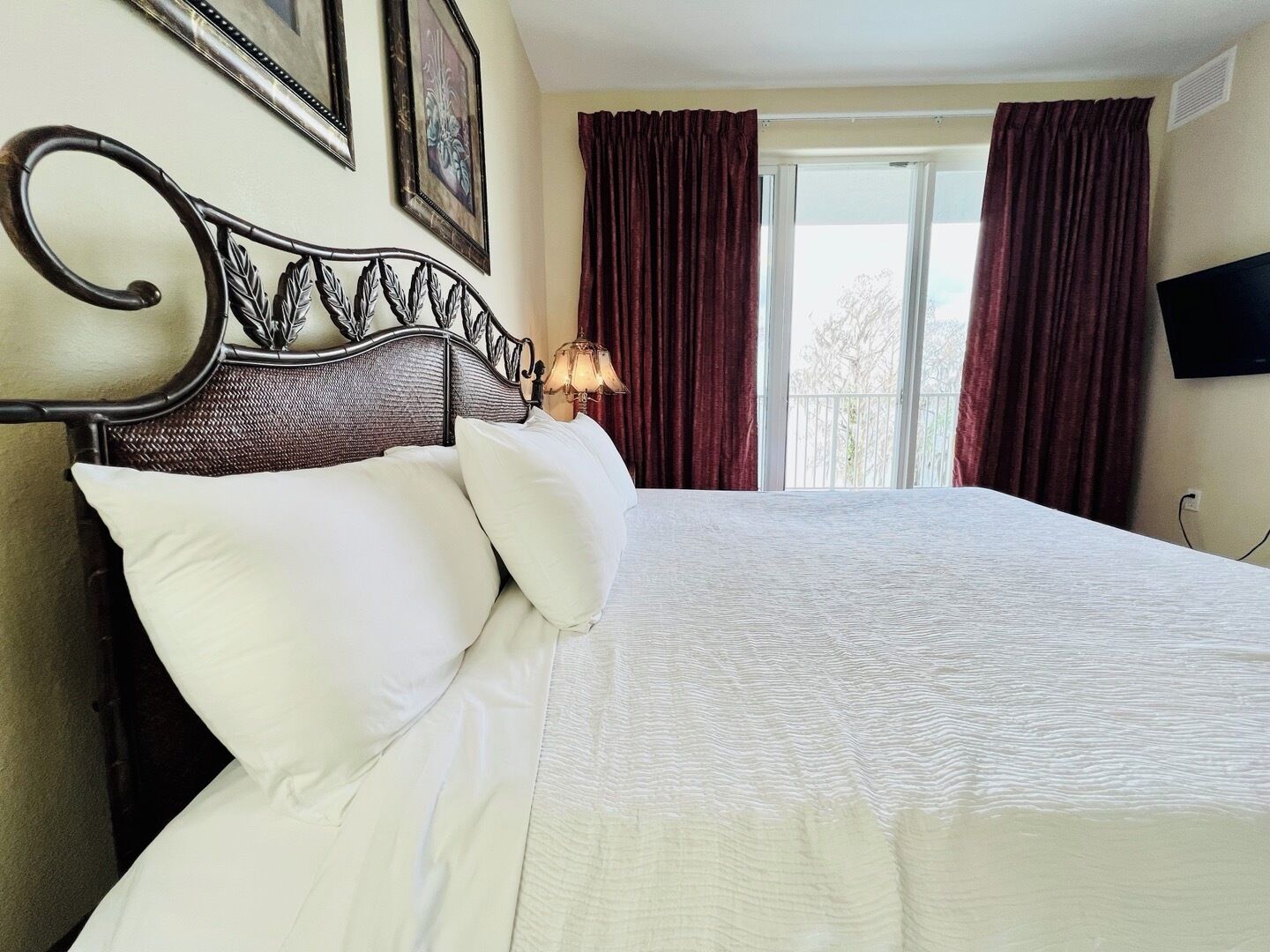 A neatly made bed with white linens and pillows, a dark metal headboard, and a window with red curtains.