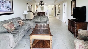 Un salon spacieux avec un canapé gris, une table basse en bois et un téléviseur posé sur un meuble en bois.