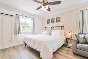 A bedroom with a large bed, a ceiling fan, a desk with a lamp, and a window with curtains. - River Escape Studio 104 (Helen)