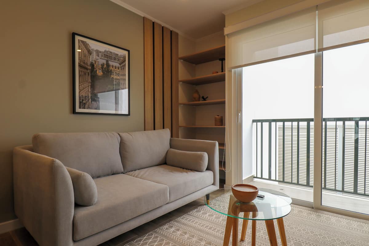 Een moderne woonkamer met een beige bank, een glazen salontafel en een ingelijste foto van een stadsgezicht aan de muur.
