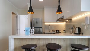 A modern kitchen with a central island, bar stools, stainless steel appliances, and pendant lighting.