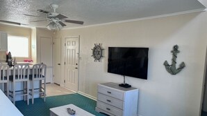 A compact living space with a kitchenette, a dining area, a flat-screen TV, and nautical decor.