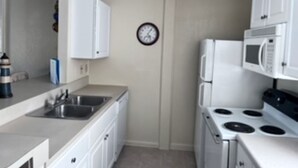 A compact kitchen with white cabinets, a microwave, a stove, and a sink.