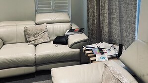 A living room with a beige leather sofa, a window with blinds, and a curtain. - Immaculate 4-bed House in Chelmsford (Chelmsford)