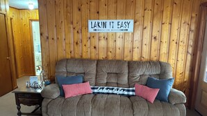En hyggelig stue med en stor, detaljeret sofa, en trævæg og et skilt med teksten "LAKIN' IT EASY".