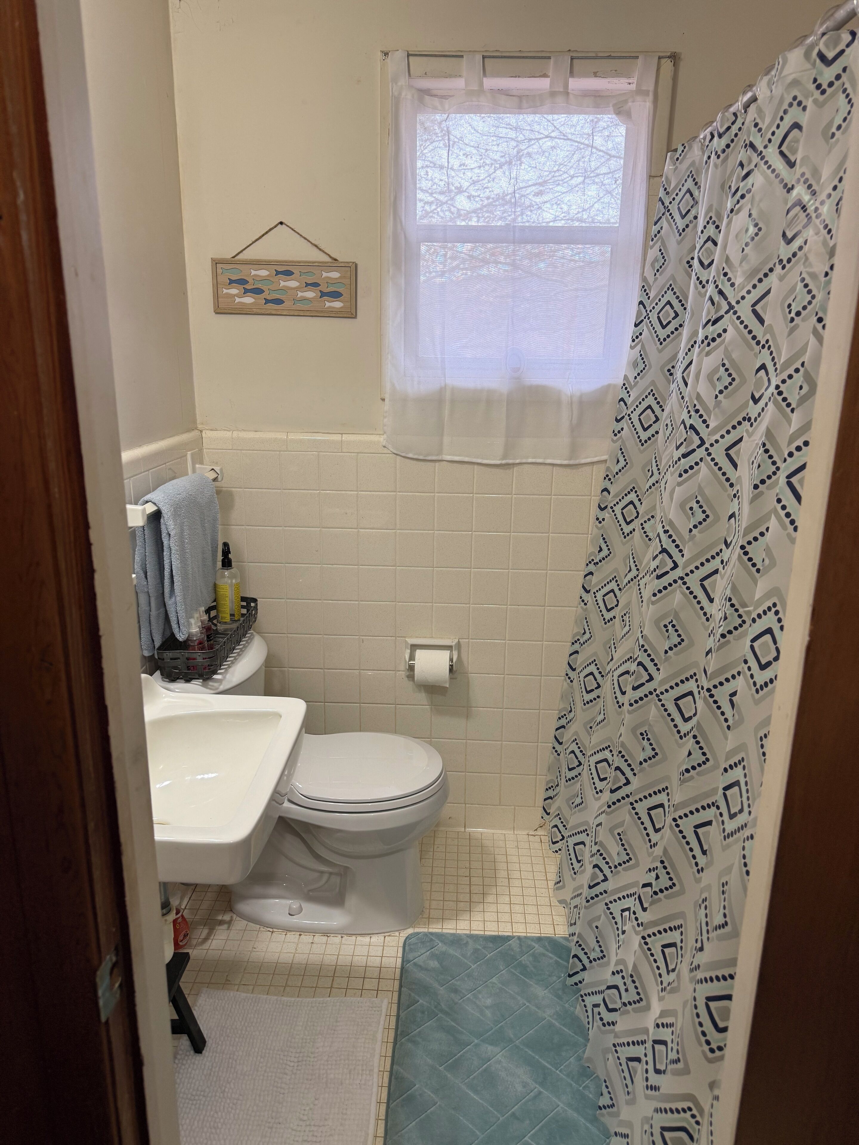 Une petite salle de bain comprenant des toilettes, un lavabo et une fenêtre agrémentée d’un rideau à motifs.