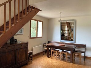 A dining area with a wooden table and chairs, a staircase, and a window with a view of greenery. - Gite 2hérault Tourisme, Piscine, Jardin, Occitanie Entre mer et Cévennes (Servian)