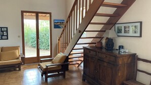 Un vaste espace de vie agrémenté d’un escalier en bois, d’un canapé, d’une armoire et offrant une vue sur un jardin, visible à travers une porte vitrée.