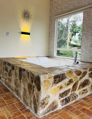 A stone bathtub with a window view of greenery.
