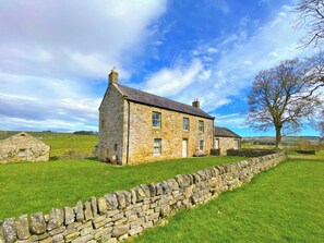 A stone house with a stone wall in front, set in a grassy field with a clear sky. - 3 bedroom accommodation in Elsdon (Elsdon)