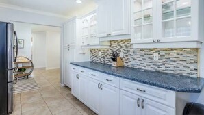 A modern kitchen with white cabinetry, a granite countertop, and a backsplash with a mosaic tile pattern. - Dog-friendly home w/ private pool & outdoor living (Cape Coral)